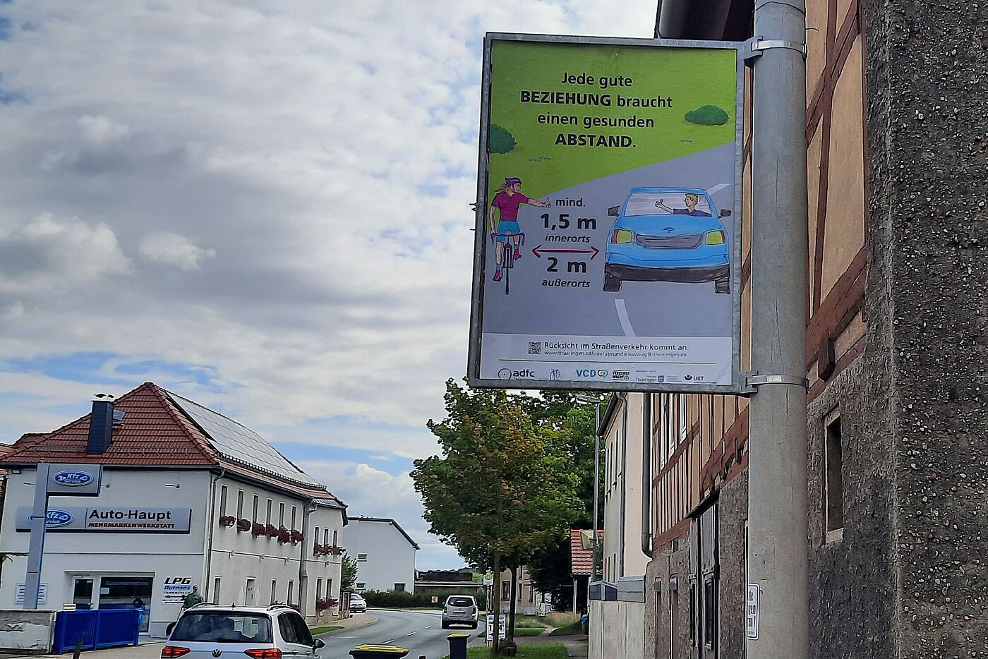 Abstandsplakat an einem Pfosten am Straßenrand.