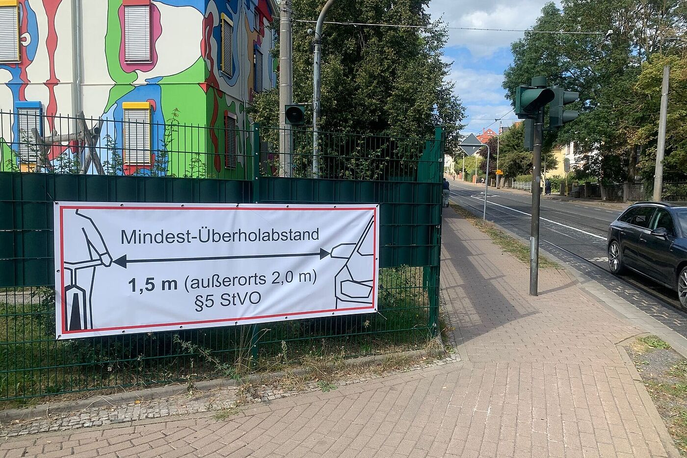 Ein Banner an einem Zaun macht auf den beim Überholen von Radfahrenden einzuhaltenden Mindestabstand aufmerksam.