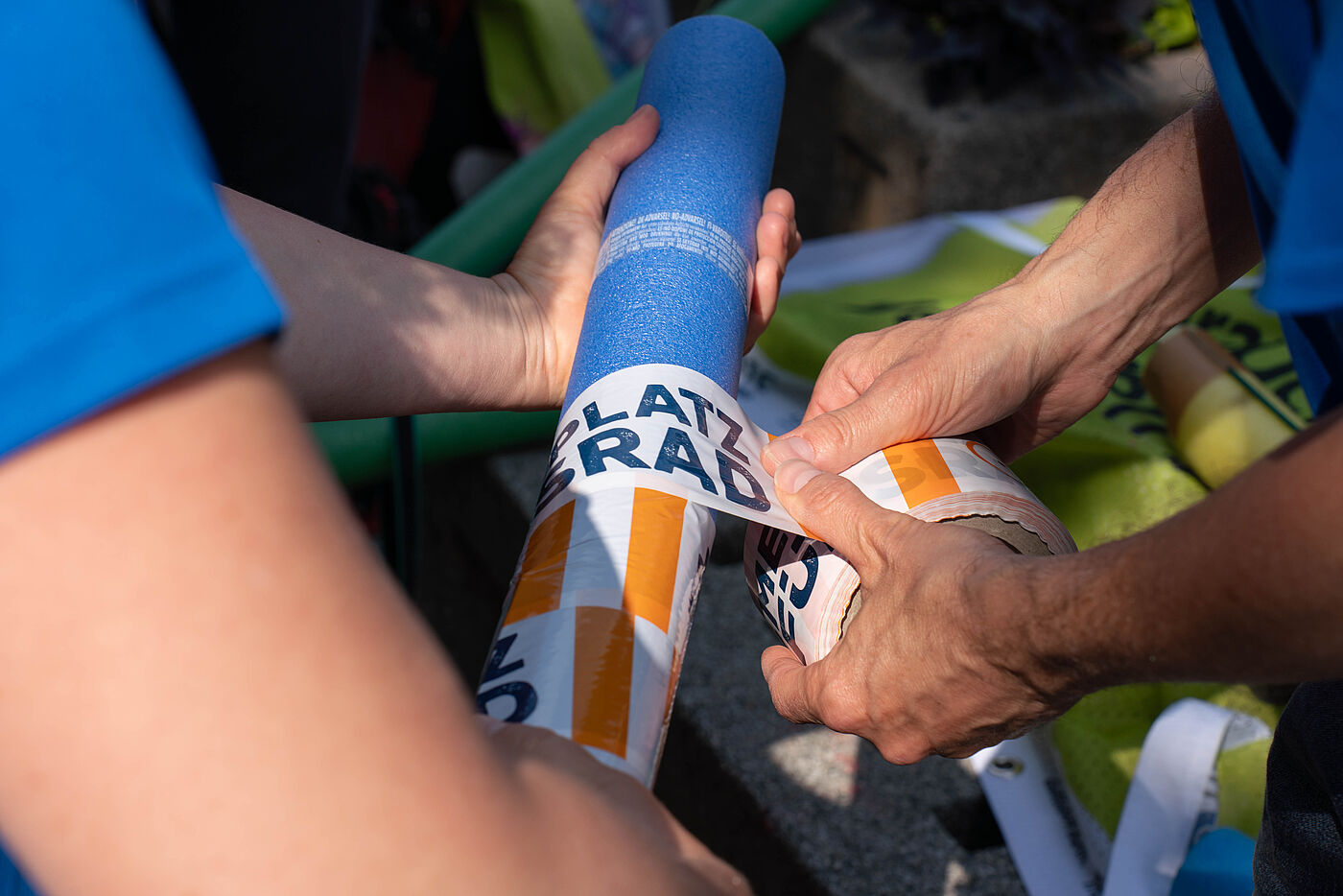 Poolnudeln werden mit Absperrband umwickelt und so für die Poolnudelaktion vorbereitet.